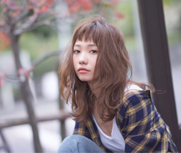 短めバングがかわいらしいヘアスタイル。レイヤーの入った毛先にゆるくパーマをかけ外国の少女のような印象に。